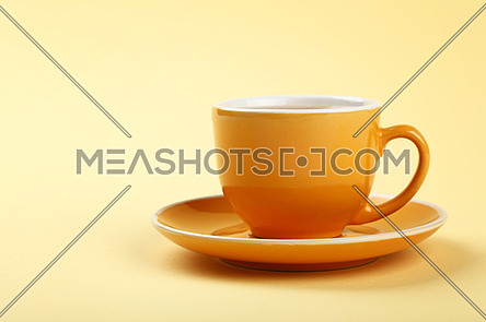 Close up one full yellow cup of tea or coffee on saucer over pastel paper background, low angle side view