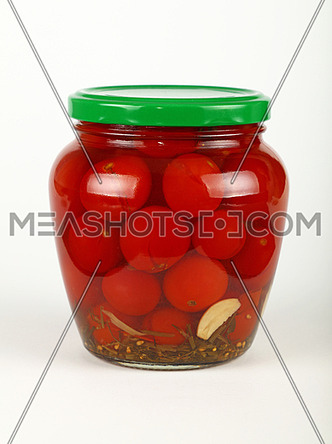 Close up of one glass jar of pickled small red cherry tomatoes with green lid over white background, low angle side view