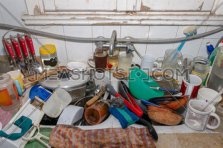 Pile of dirty utensils in a kitchen washbasin