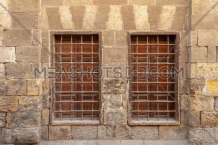 Two similar adjacent wooden windows with iron grid over decorated stone bricks wall, Medieval Cairo, Egypt