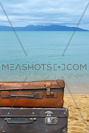 Close up stack of two old vintage antique grunge travel luggage brown leather suitcase trunks isolated over background of sea beach, low angle side view
