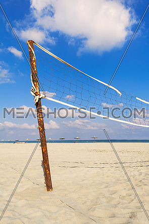 Torn volleyball net on the beach with cloudy blue sky and yellow sand in the morning