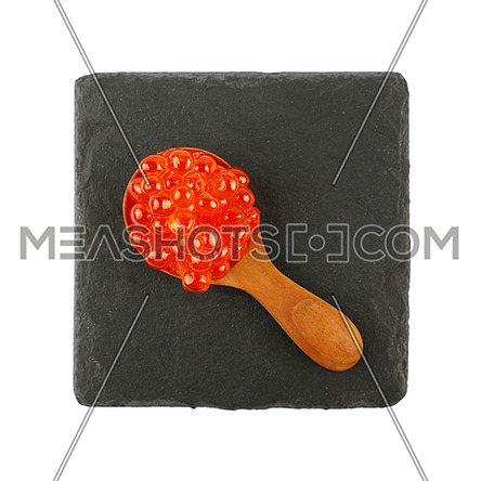 Close up one portion of salmon fish red caviar in wooden scoop spoon on black slate serving board isolated on white background, elevated top view, directly above