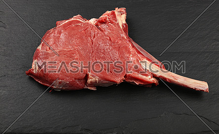 Close up one raw tomahawk ribeye beef steak with rib bone on black slate board background, high angle view