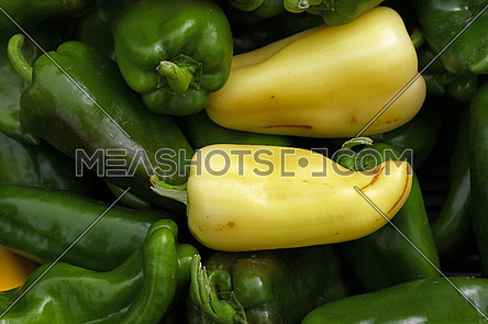Close up background of fresh green and yellow sweet bell peppers on retail display of farmers market, high angle view, personal perspective
