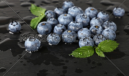 Close up fresh washed blueberry berries with water drops and green mint leaves on black slate board, high angle view