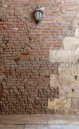 Front view of grunge weathered uneven red stone bricks wall and one lantern, Medieval Cairo, Egypt