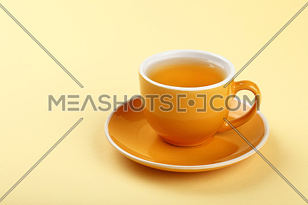 Close up one full yellow cup of green oolong or herbal tea on saucer over pastel paper background, high angle view