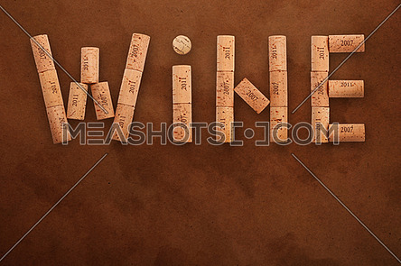 Word WINE shaped by natural wooden wine bottle corks of different vintage years over background of dark brown paper parchment