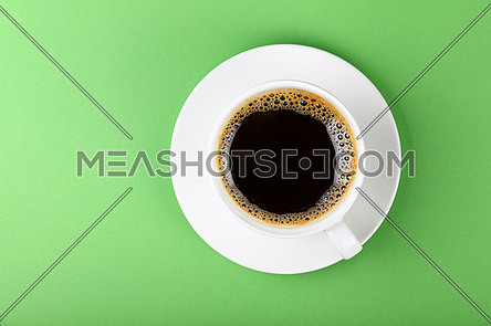 Close up one full white cup of black Americano coffee and saucer over pastel green paper background, elevated top view, directly above
