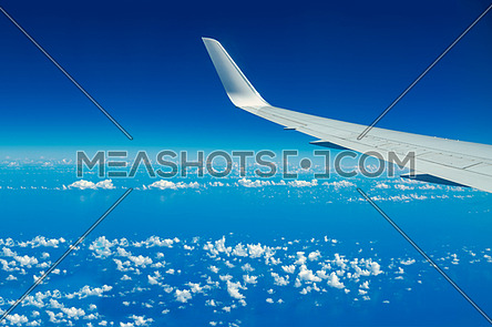 Looking through aircraft window during flight. Aircraft wing over blue skies and white clouds.Copy space.