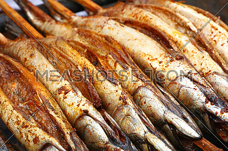 Close up cooking several bonito mackerel fishes on wooden skewer grill, high angle view