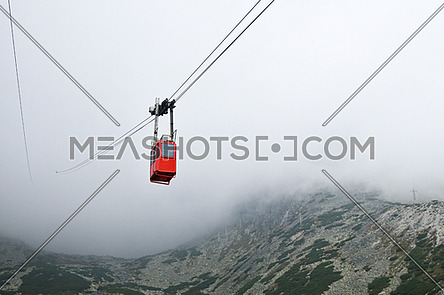 Red mountain cableway car lift in clouds and fog, low angle view