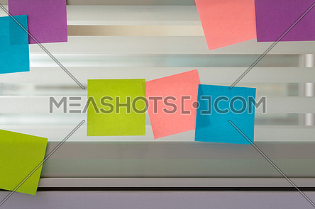 Three colored sticky notes surrounded by randomly scattered sticky notes over glass screen of a bench desk
