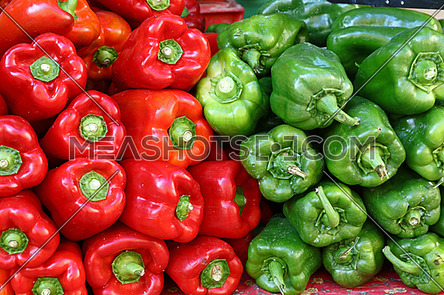 Close up background of fresh green and red sweet bell peppers on retail display of farmers market, low angle view