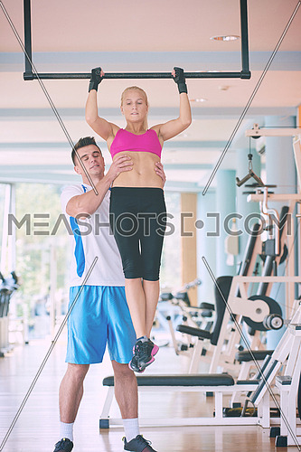 trainer support young woman while lifting on bar in fitness gym indoors