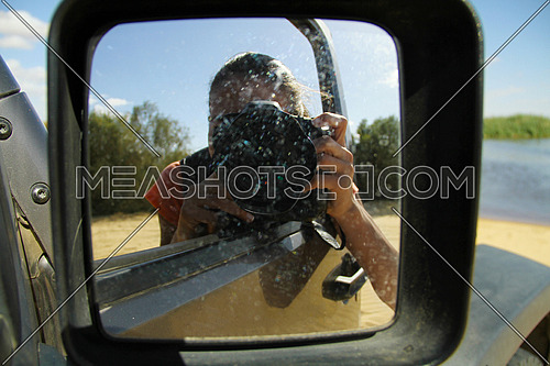 Cute young middle eastern female photographer with camera. Woman reflected in the rearview mirror of a car on a summer day
