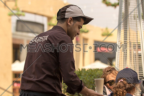 A barista dressed in brown uniform serving hot coffee in an outdoor area of a coffeshop