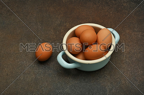 Close up pan bowl of brown chicken eggs on dark grunge table surface, high angle view
