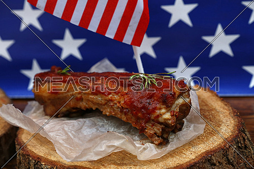 Portion of cooked pork spare ribs in bbq sauce on paper parchment and wood cut under American flag, close up, high angle view