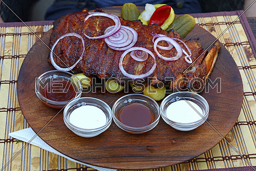 Rack of grill roasted pork spare ribs with onion rings, pepper and sauces, close up, high angle view, personal, perspective