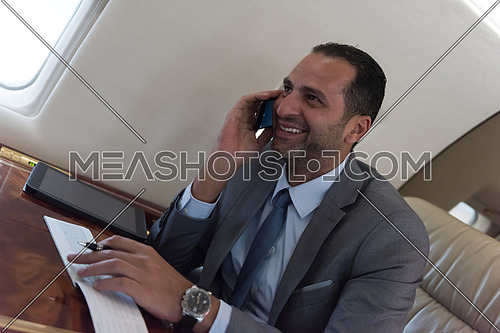 young middle eastern successful businessman talking on the phone while sitting in a private airplane