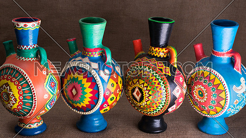 Still life of four decorated colorful handcrafted pottery jugs on sackcloth background, one of the art works of Ebtessam ElGohary, a contemporary Egyptian artist specialized in pottery painting art