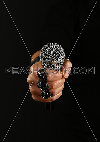 Close up man hand with metal rings and bracelet holding microphone over black background, side view