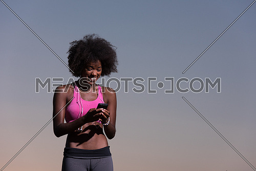 portrait of a young beautiful african american woman with headphones and mobile phone jogging in nature beautiful summer night