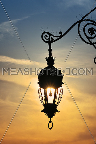 Close up side view of old vintage antique street lamp lantern over bright evening sunshine and vivid sunset sky