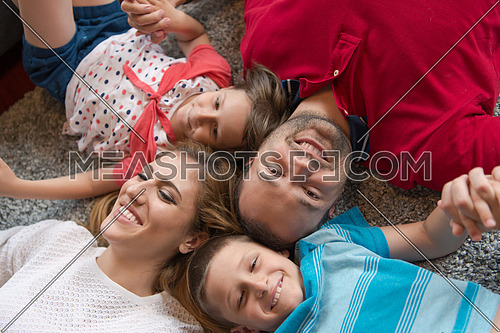 Top view of beautiful young parents, their cute little daughter and son holding hands, looking at camera and smiling, lying on the floor