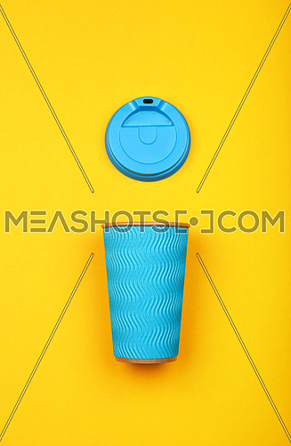 Close up one crimped disposable pastel blue paper takeaway coffee cup with plastic cap over vivid yellow background, flat lay, elevated top view, directly above