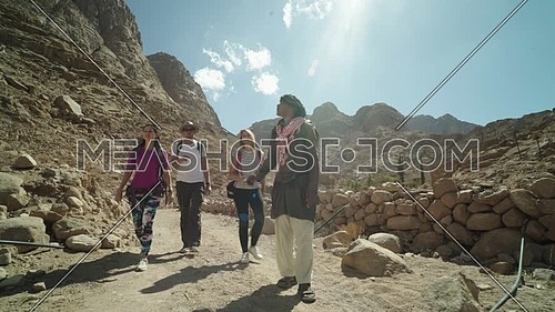 Reveal shot for group of tourists walking with bedouin guide exploring Sinai Mountain from wadi Freij at day.