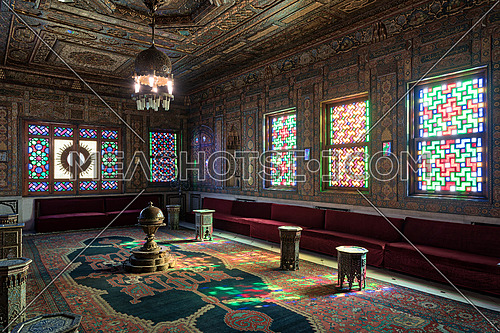 Cairo, Egypt - December 2 2017: Manial Palace of Prince Mohammed Ali. Syrian Hall with ornate wooden wall and ceiling, windows with colored stained glass and Ottoman Empire logo, old ornate chandelier, red couches, tea tables and ornate carpet