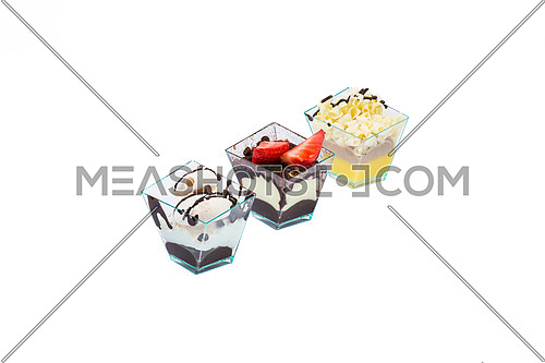 Arranged in a row diagonally,three cupcakes with choccolate,white choccolate, fruits,cream and custard in a plastic cup,isolated on white background.