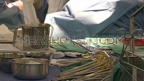 Close shot for Nurse organizing surgical instruments on tray during heart surgery is performing in background