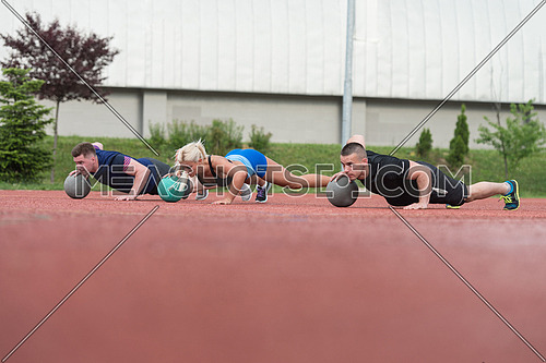 A Group Of Young People In Aerobics Class Performing Push-Ups On Medicine Ball Exercise Outdoor