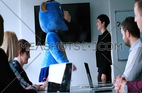 Boss dressed as teddy bear having fun with bussines people in modern corporate office