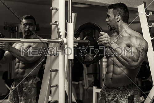 Body Builder Putting Weights On Bar In Gym