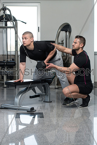 Personal Trainer Showing Young Man How To Train Back Exercise With Dumbbell In A Health And Fitness Concept