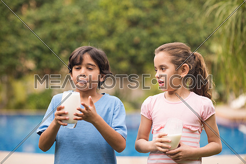 Middle Eastern boy and girl enjoying with a glass of milk in their hands outside on summer day