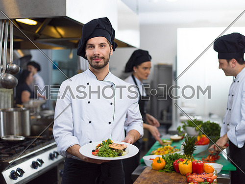Chef holding fried Salmon fish fillet with vegetables for dinner in a restaurant kitchen