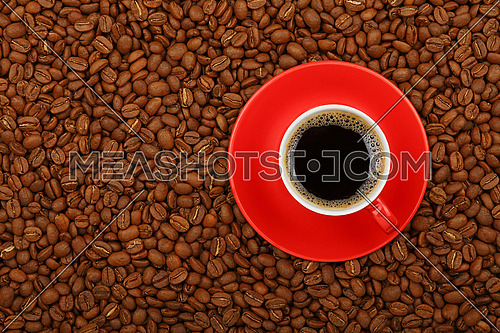Full Americano black filtered coffee in red cup with saucer on background of roasted coffee beans, elevated top view, close up