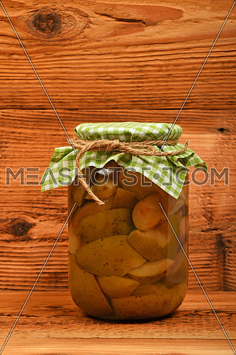 One big glass jar of homemade pear compote with green checkered textile top decoration at brown vintage wooden surface