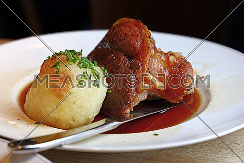 Portion of roasted succulent pork fore shank or knuckle with Bavarian dumplings and chive in plate on table, close up, low angle view