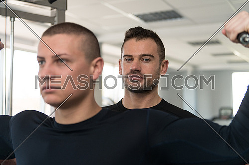 Personal Trainer Showing Young Man How To Train Biceps On Machine In The Gym