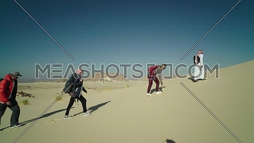 Follow shot for group of tourists walking on sands with bedouin guide while exploring Sinai Trail from Ain Hodouda at day.
