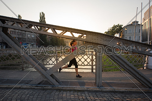 young sporty woman jogging across the bridge at sunny morning in the city