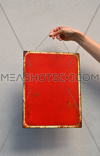 Close up woman hand holding red metal painted empty warning sign with copy space over concrete wall