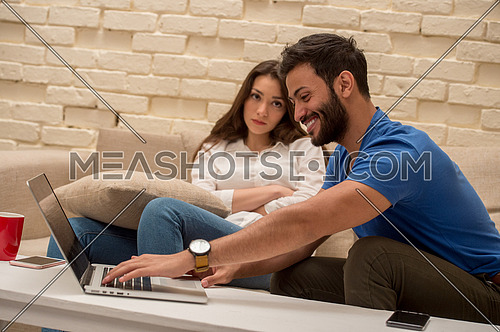 A young man and young lady sitting at home using a laptop